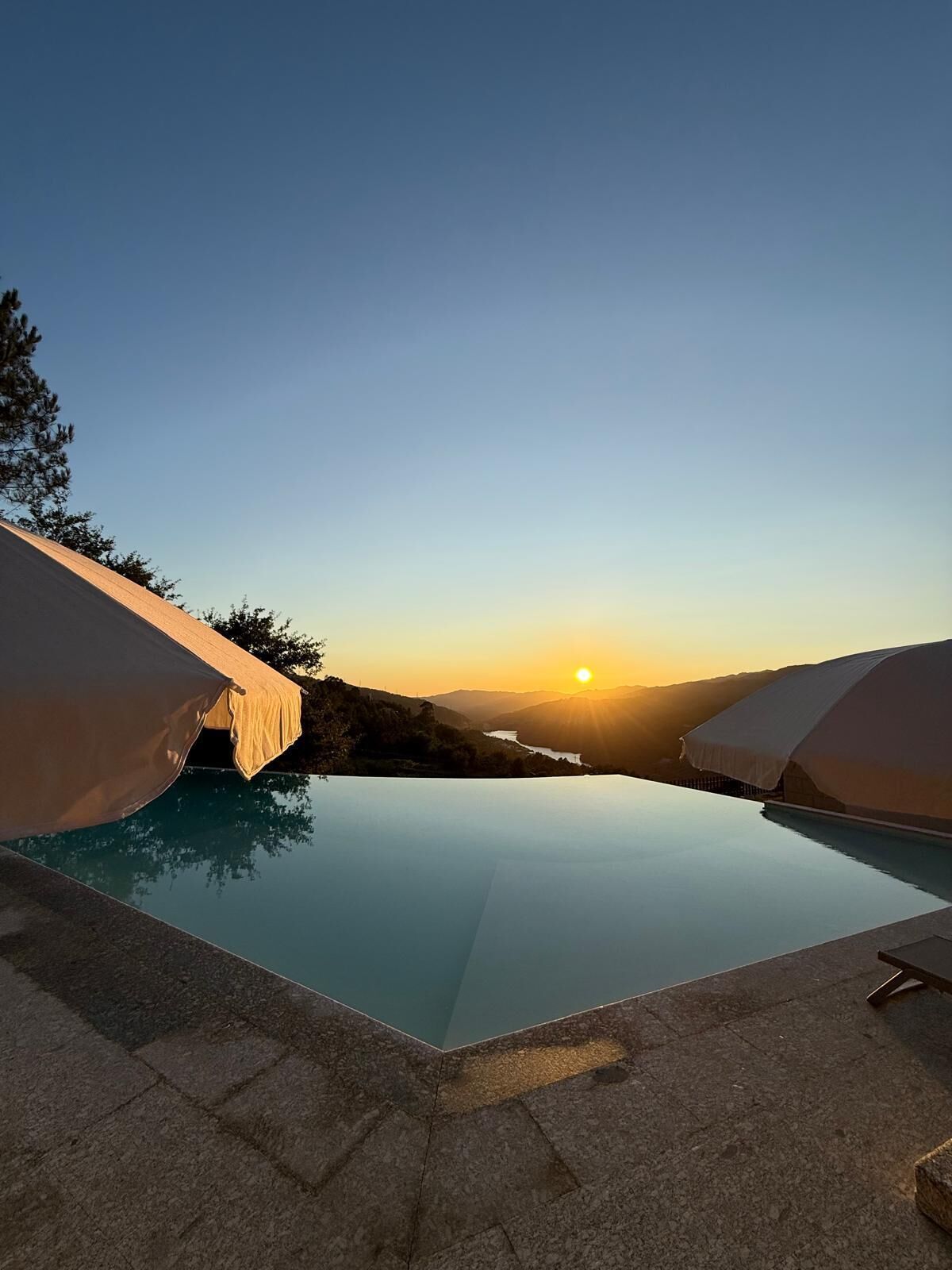 An infinity pool with a clear view of the sunset over a mountainous landscape.