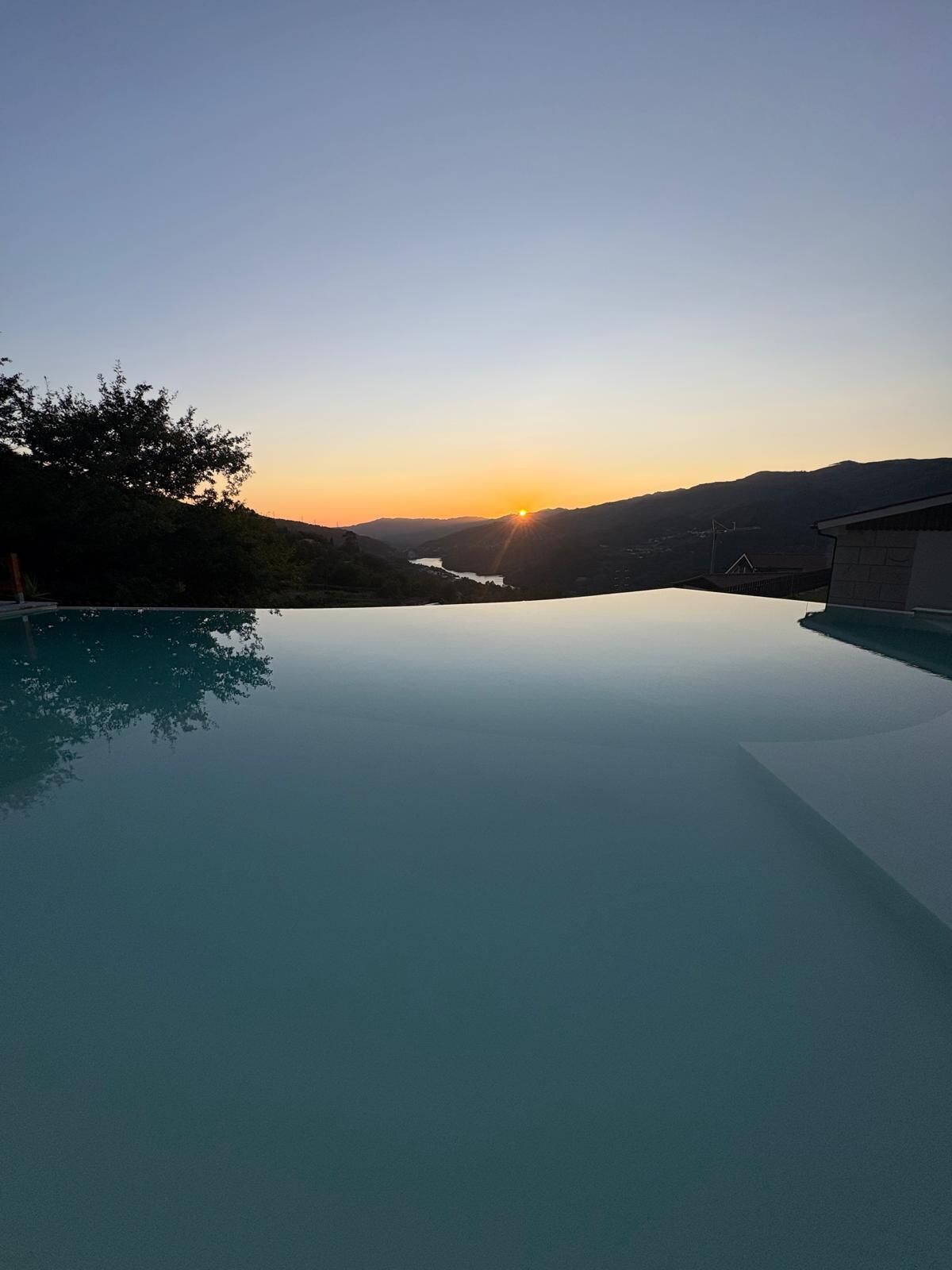 Un ciel dégagé avec un coucher de soleil sur une étendue d’eau, le tout entouré de collines.
