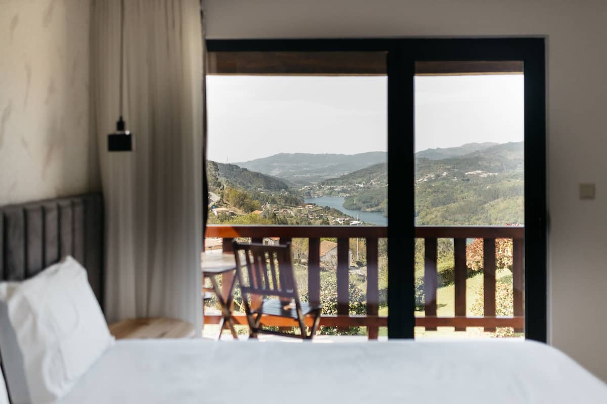 Un dormitorio con cama, una silla y vistas a un paisaje montañoso a través de una puerta abierta.