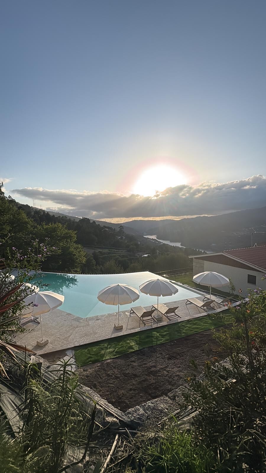 Una piscina con lettini e ombrelloni, circondata dal verde e con vista sul paesaggio.