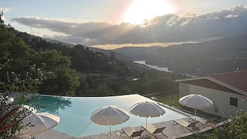 Una piscina con lettini e ombrelloni, circondata dal verde e con vista sul paesaggio.