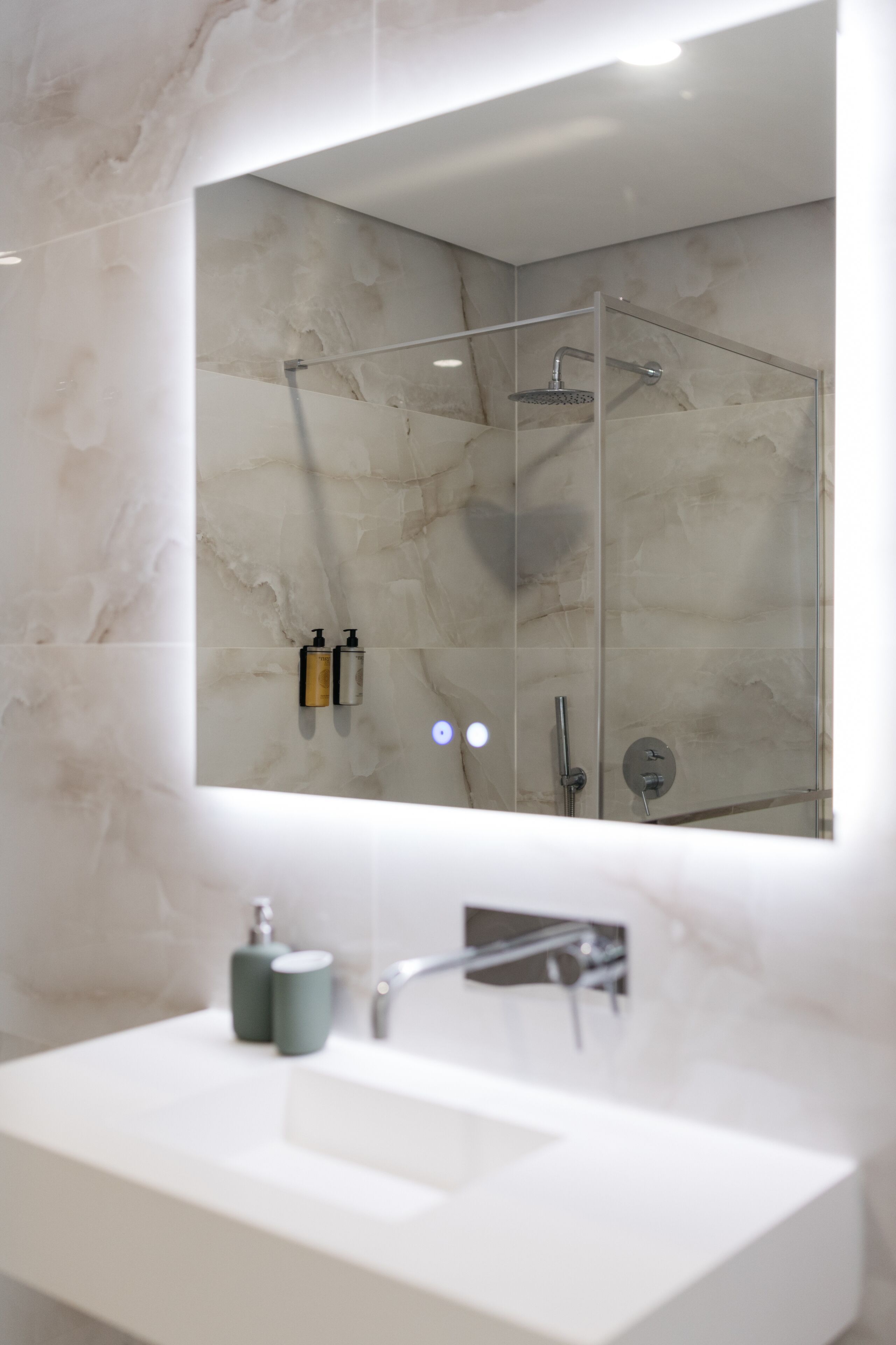 A modern bathroom with a large mirror, a white sink, and a glass-enclosed shower area.