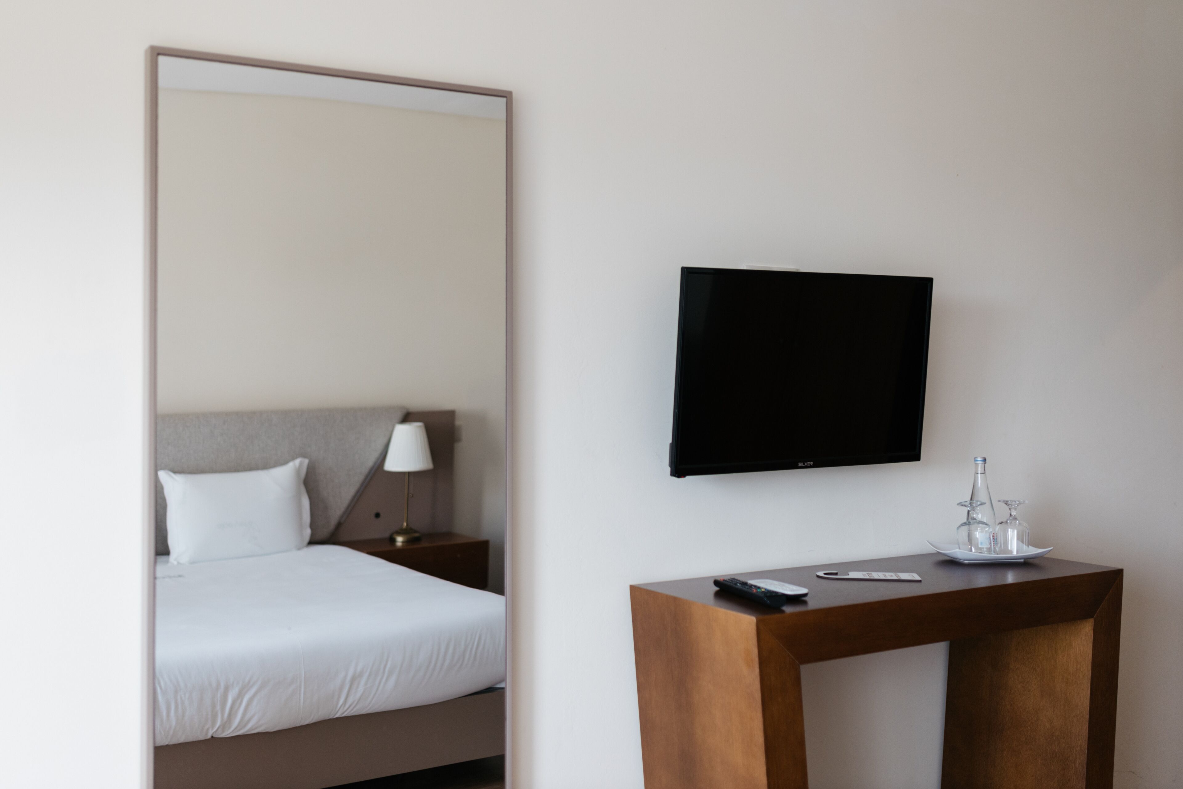 Een hotelkamer met een bed, nachtkastje, televisie en een klein tafeltje met afstandsbediening en een set glazen.