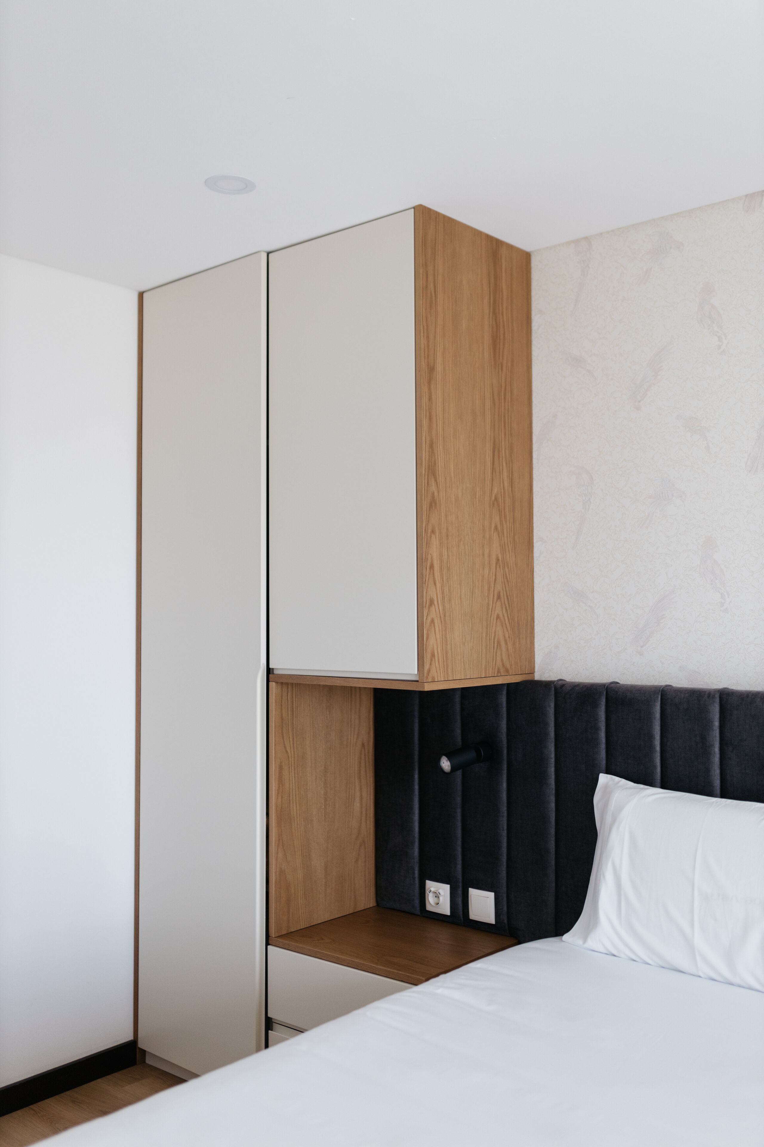 A modern hotel room with a bed, a wooden wardrobe, and a headboard.