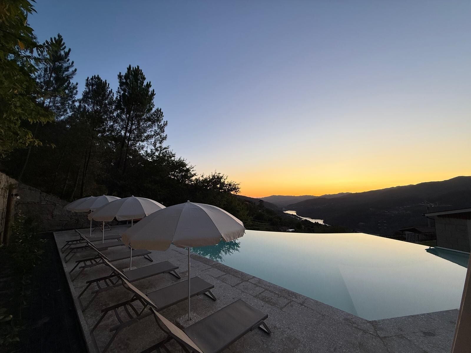A poolside area with lounge chairs and umbrellas, overlooking a valley and mountains.