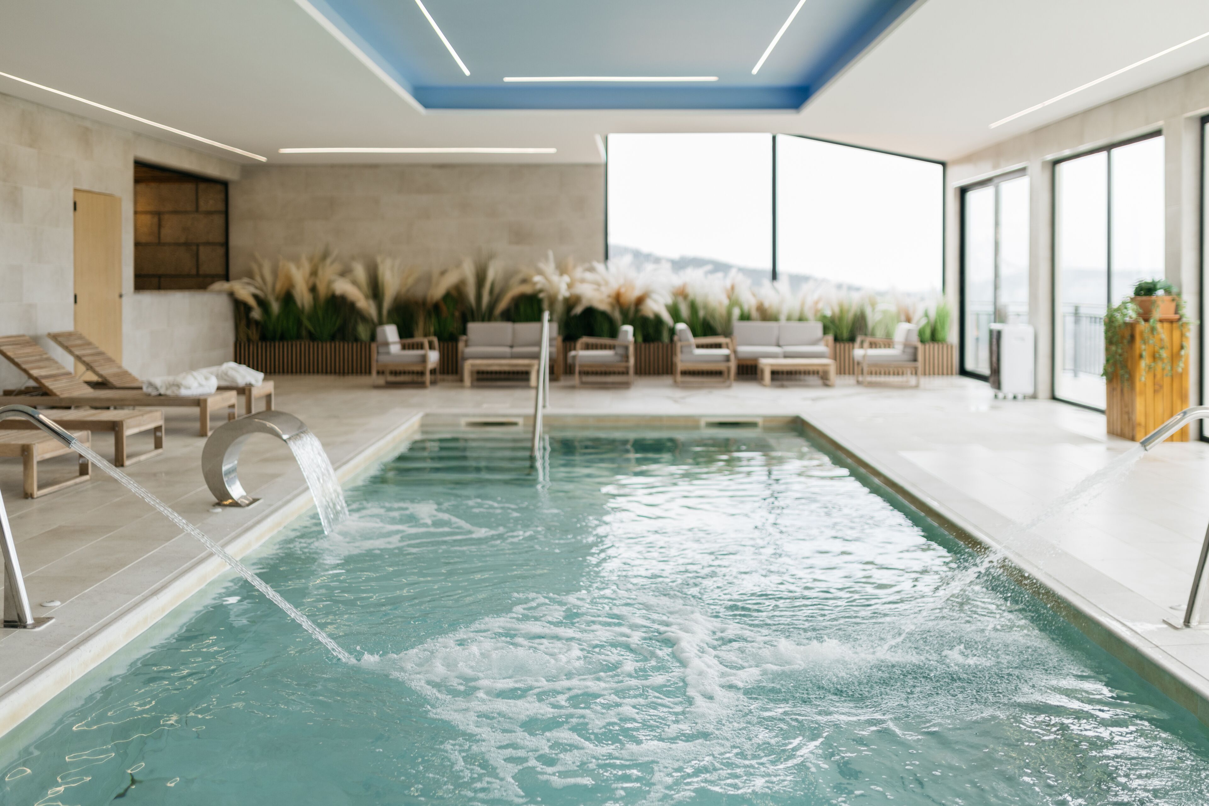 A modern indoor pool with clear water, surrounded by lounge chairs and a view of the mountains.