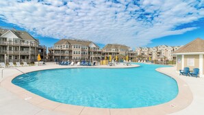A swimming pool surrounded by multi-story buildings with balconies, lounge chairs, and umbrellas. - Gorgeous ocean views from this stunning, updated coastal condo! (Duck)