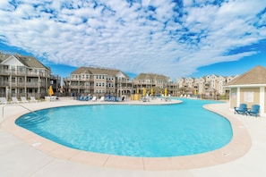 A swimming pool surrounded by multi-story buildings with balconies, lounge chairs, and umbrellas.