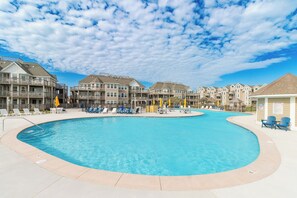 Une piscine entourée d’immeubles à plusieurs étages, dotés de balcons, de chaises longues et de parasols.