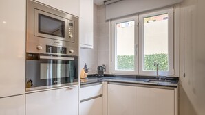 A modern kitchen with stainless steel appliances, a window with a view of greenery, and a built-in oven. - Modern 1-Bed Apartment with Private Terrace (Madrid)