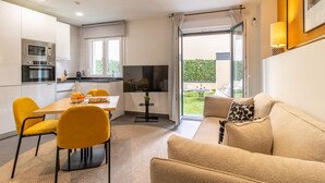A modern kitchen with built-in appliances, a dining area with yellow chairs, and a sofa with patterned cushions. - Modern 1-Bed Apartment with Private Terrace (Madrid)