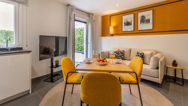 A modern living room with a sofa, yellow chairs, a dining table with fruit and drinks, a TV, and a window with curtains. - Modern 1-Bed Apartment with Private Terrace (Madrid)