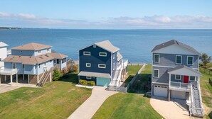 Un quartier résidentiel bordé de maisons au bord de l’eau, avec une maison bleue au centre, dotée d’un garage, une maison grise avec une porte rouge et une maison blanche avec un balcon.