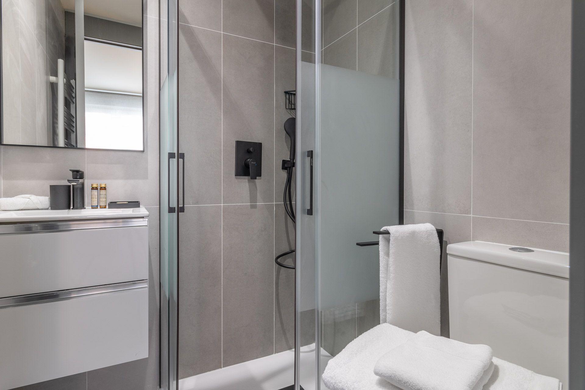 A modern bathroom with a glass-enclosed shower, a white toilet, and a sink with a mirror.