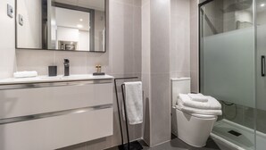 A modern bathroom with a glass shower enclosure, a white toilet, and a vanity with a mirror and a microwave.
