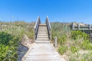 A wooden boardwalk leading to a sandy beach area with vegetation on either side. - Oceanfront condo in Nags Head w/ community pool just steps to the sand! (South Nags Head)