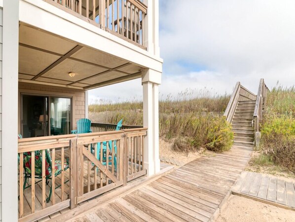 A two-story building with a wooden deck and a staircase leading to a beach. - Oceanfront condo in Nags Head w/ community pool just steps to the sand! (South Nags Head)