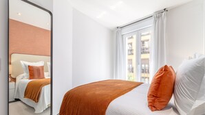 Ett hotellrum med en stor säng, en spegel, ett fönster med gardiner och utsikt över byggnaderna utanför.