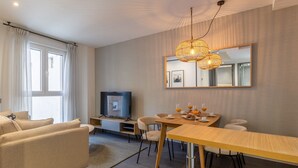 Een moderne woonkamer met een bank, een televisie, een eettafel met stoelen en een grote spiegel aan de muur.