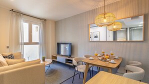 Een moderne woonkamer met een bank, een eettafel gedekt voor het ontbijt, een televisie en een grote spiegel.