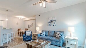 A modern living room with a blue sofa, wooden coffee table, and a ceiling fan. - Great Coastal Condo in the heart of Kill Devil Hills NC! (Kill Devil Hills)