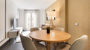 A modern hotel room with a round dining table, beige chairs, a TV on a stand, a lamp, and a potted plant. - Amazing new duplex for 4 (Madrid)