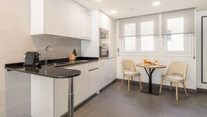 A modern kitchen with a black countertop, stainless steel sink, and a built-in oven. There is a dining area with two chairs and a table, and a window with blinds. - Amazing new duplex for 4 (Madrid)