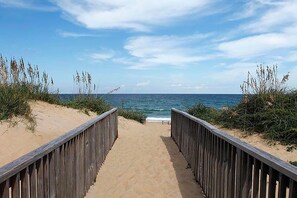 A wooden boardwalk leading to the beach with sand and vegetation on either side. - Nags Head vacation rental steps from the beach with rec room! (Nags Head)