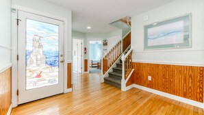 A hallway with wooden flooring, a wooden wainscoting wall, a staircase with wooden railings, and a door with a stained glass design.