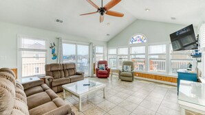 A spacious living room with a ceiling fan, large windows, a comfortable sofa, and a television.