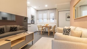 Un salon moderne avec un canapé, une table basse et un téléviseur. Il y a également un coin cuisine avec une table à manger et des chaises.