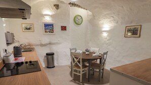A compact kitchen with a dining area, featuring a stove, sink, and a clock on the wall. - Le Durkestrete Cellar (Haverfordwest)