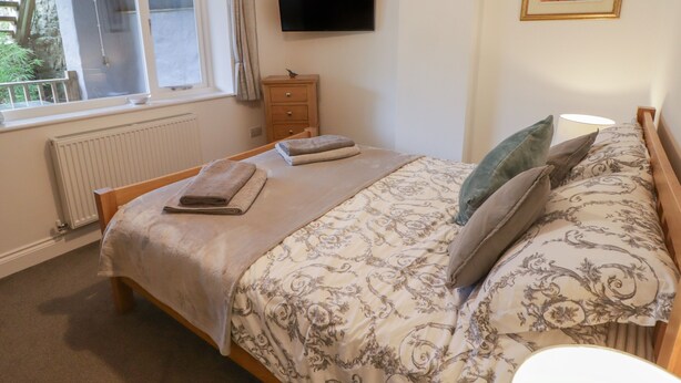 A bedroom with a bed, a window, a TV, a bedside table, and a framed picture on the wall. - Le Durkestrete Cellar (Haverfordwest)