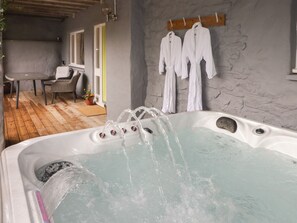 Zona de spa con jacuzzi, suelo de madera y batas blancas colgadas en la pared.