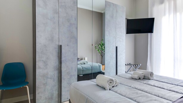 A modern hotel room with a large bed, a blue chair, a flat-screen TV, and a mirror.