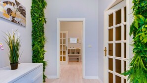A hallway with a wooden floor, a white door with glass panels, and green plants on the walls.