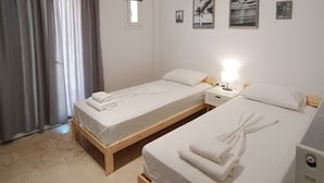 Une chambre avec deux lits simples, une petite fenêtre et un mur orné de trois tableaux encadrés.
