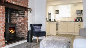 A cozy living room with a fireplace, a comfortable armchair, and a fluffy ottoman. - Henllys (Harlech)