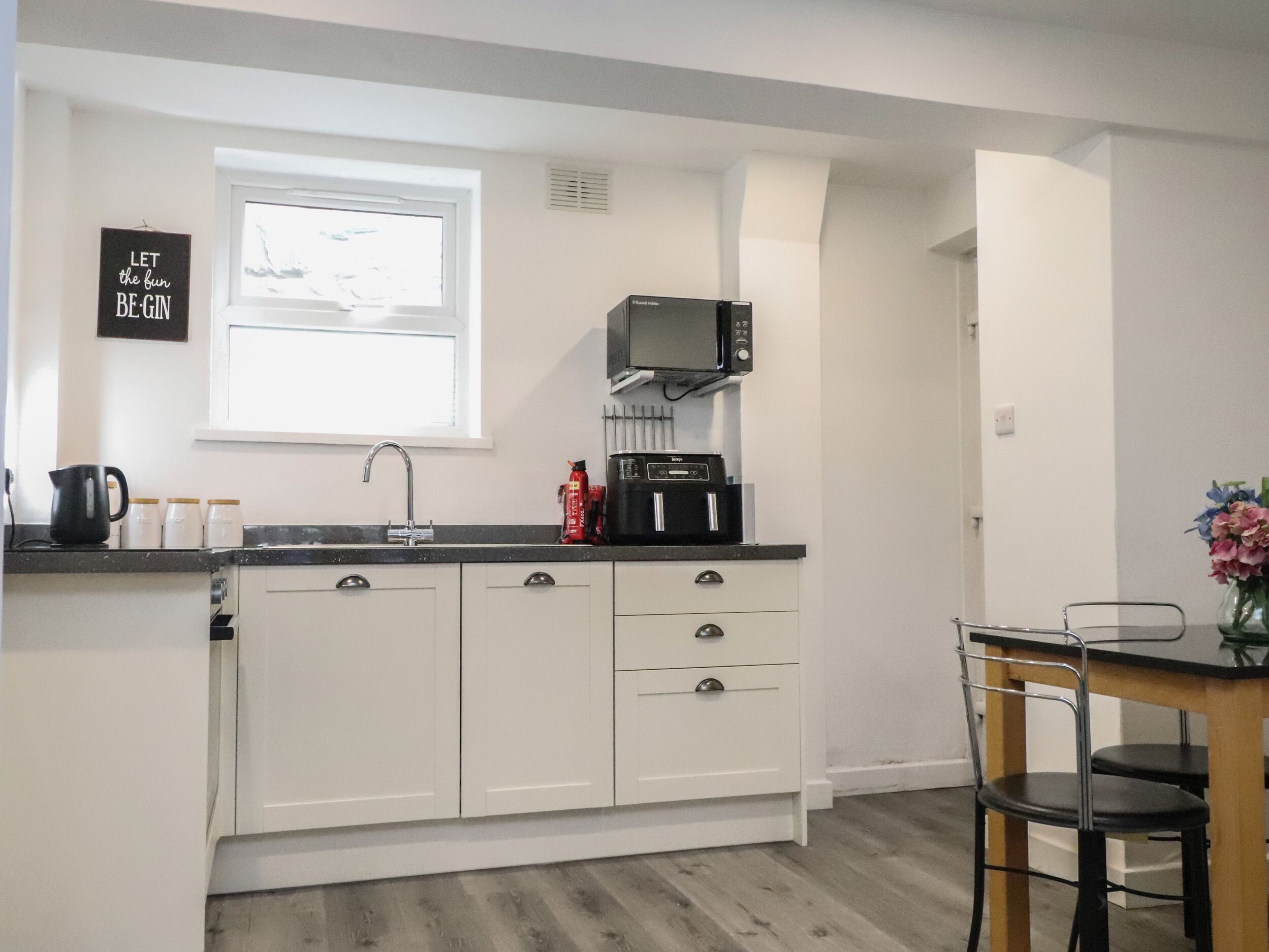 Una cocina compacta con armarios blancos, un microondas negro y un ventanal sobre el lavabo.