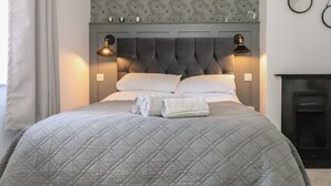 A neatly made bed with a quilted grey bedspread, two pillows, and rolled white towels. - Henllys (Harlech)
