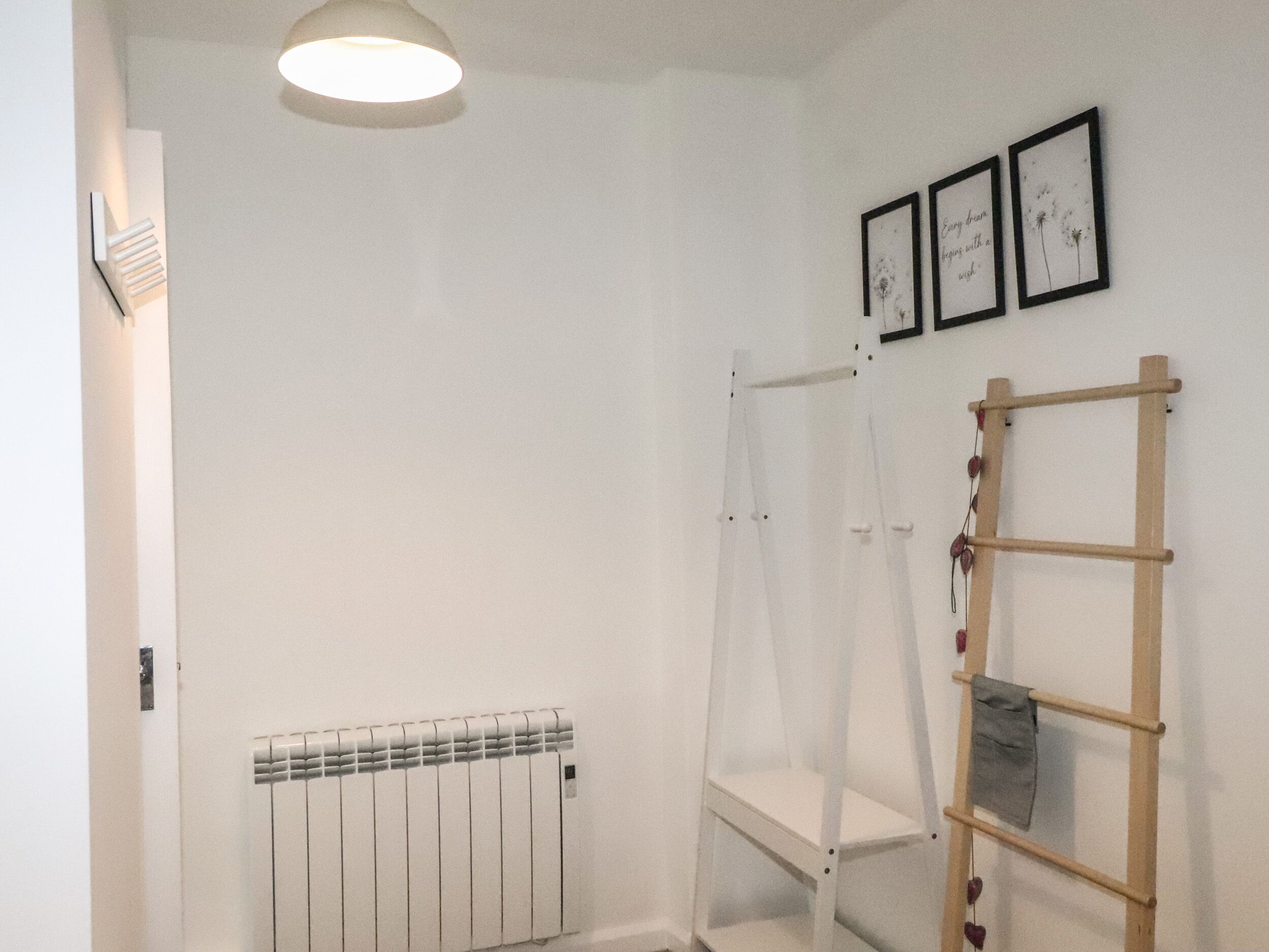 A white room with a radiator, a wooden ladder, and three framed pictures on the wall.