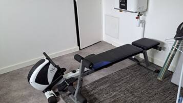 Et lille, nødtørftigt møbleret rum med bænk, motionscykel og radiator.