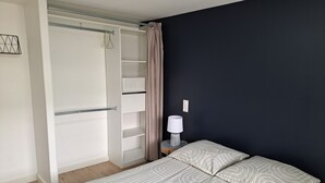 A bedroom with a bed, a wardrobe, a bedside table with a lamp, and a wall-mounted light switch. - Appartement Refait à Neuf Tout Équipé en RDC Avec Jardin Terrasse ,barbecue (Avrillé)