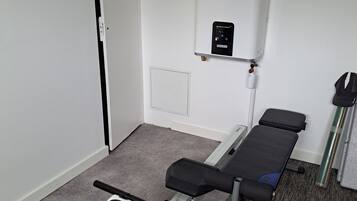 Ett litet, sparsamt möblerat rum med en bänk, en massagestol och en väggmonterad värmare.
