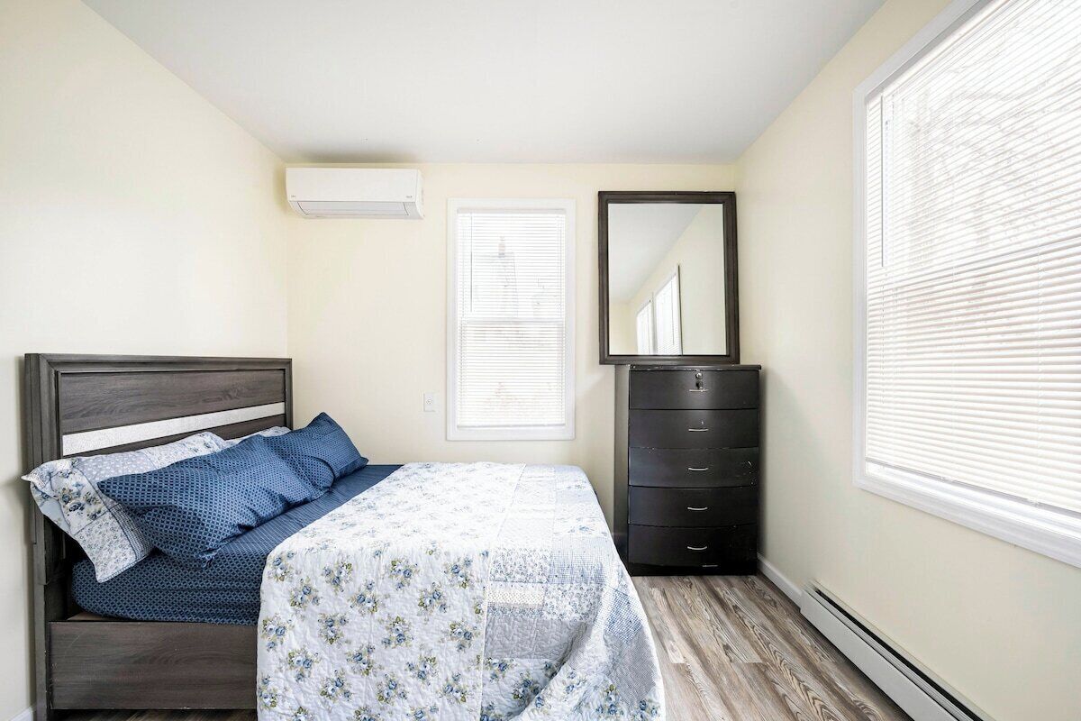 A bedroom with a bed, dresser, and window with blinds.