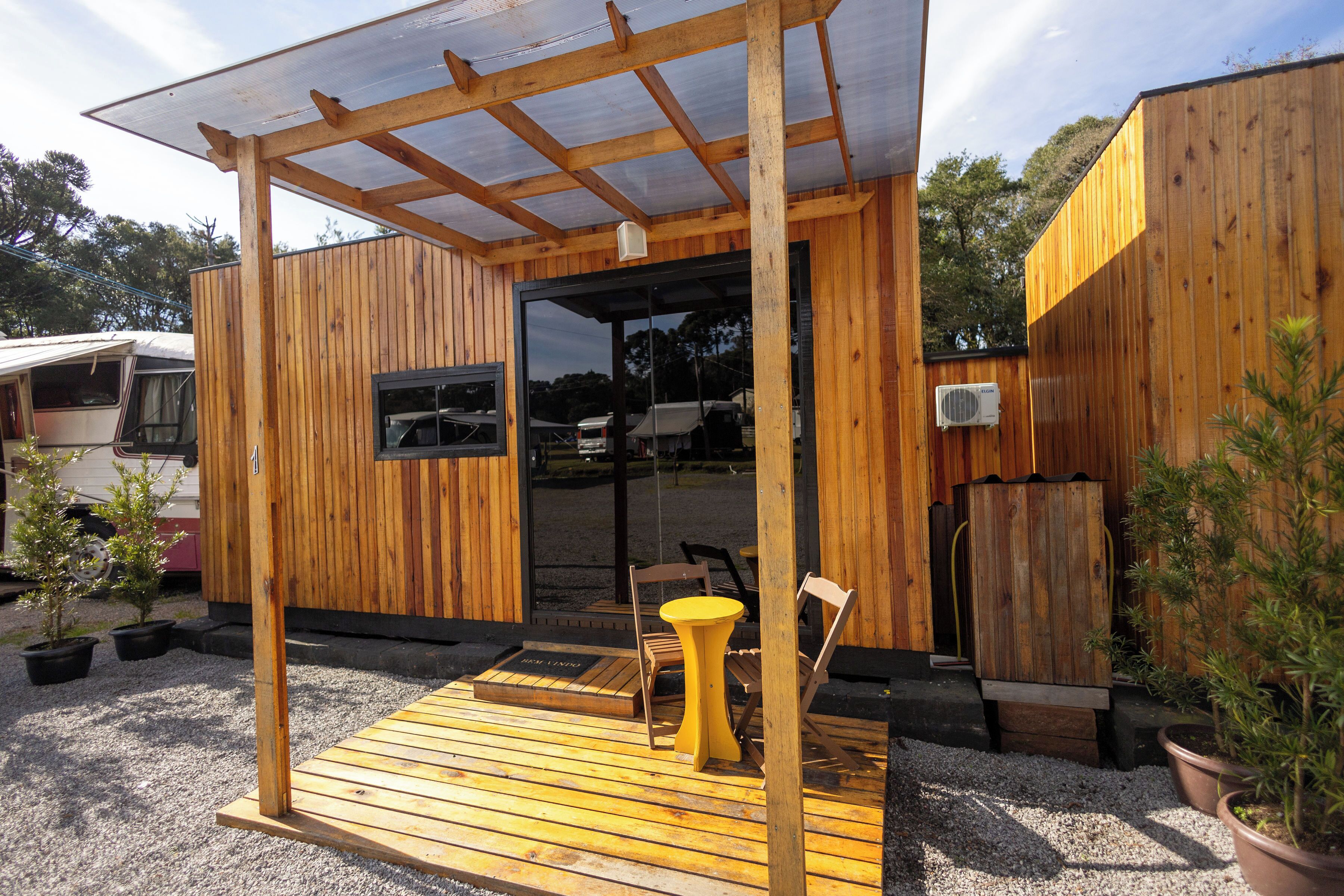 Una estructura de madera con un porche cubierto, una mesa y sillas, y plantas en macetas.