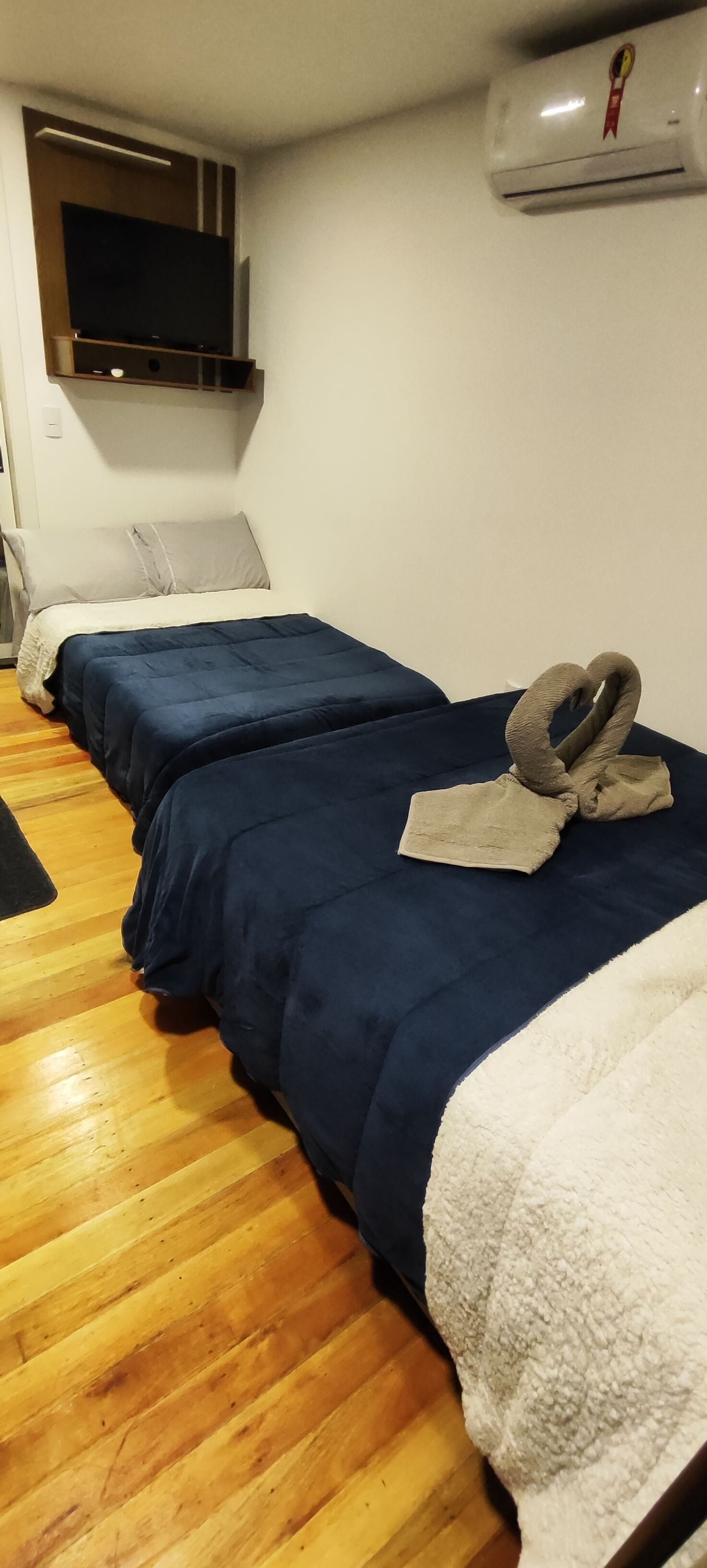 Una habitación de hotel con dos camas, un televisor montado en la pared y un equipo de aire acondicionado.