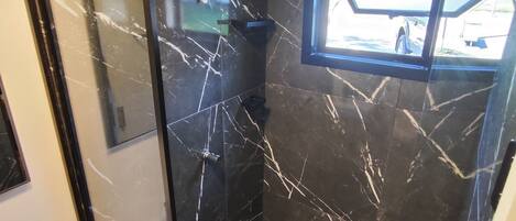 A modern bathroom with black marble walls and a glass shower enclosure.