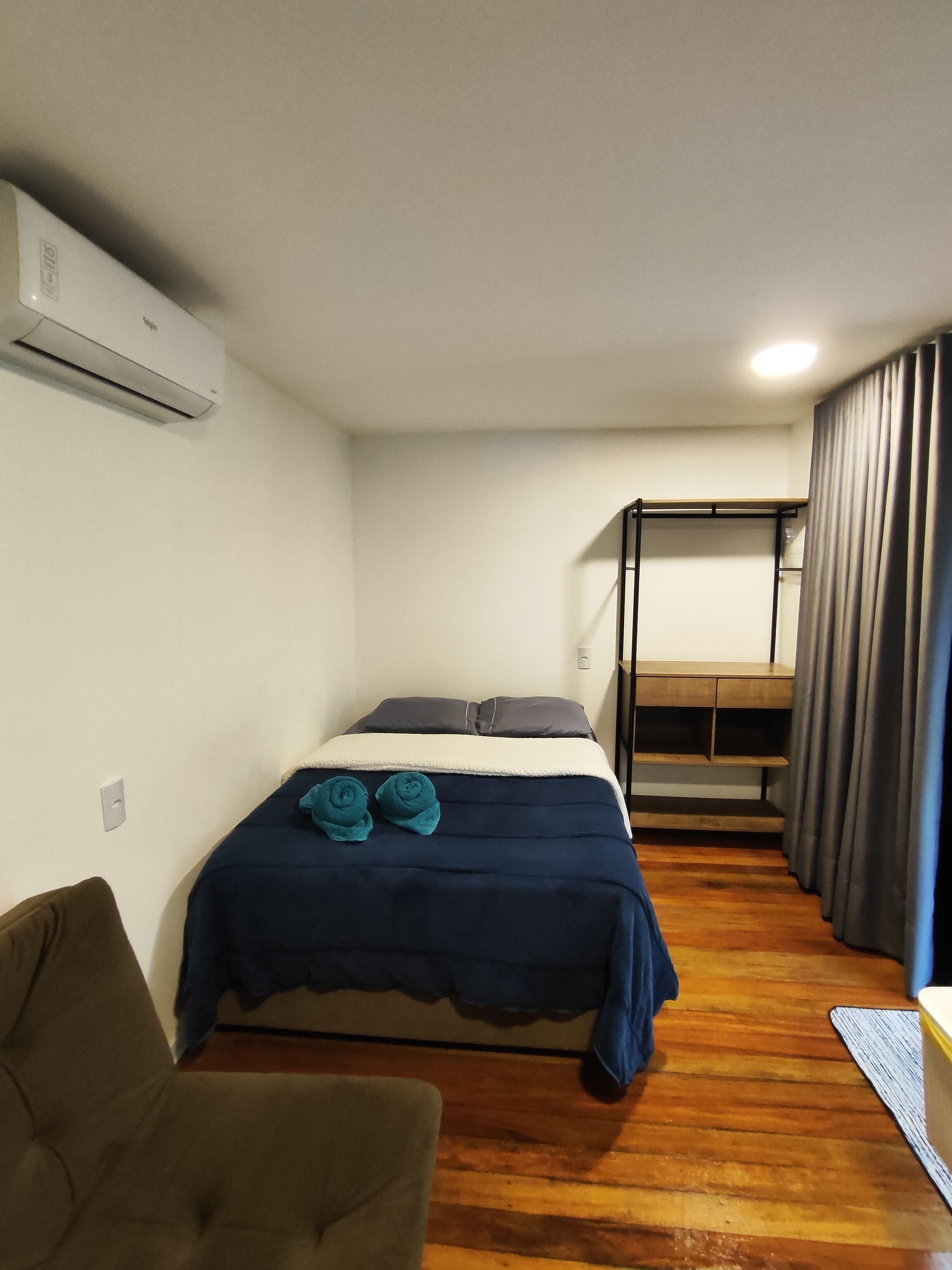 Una habitación compacta con cama, un pequeño sofá, un banco empotrado y una ventana con cortinas.