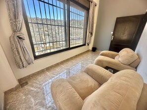 A room with a large window, a dark wooden door, and a beige sofa. - Villa Mira Guesthouse - Downtown Amman (Amman)
